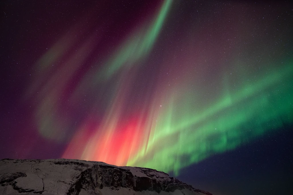 Vibrant magenta and violet solar flares cutting through the Arctic night horizon.