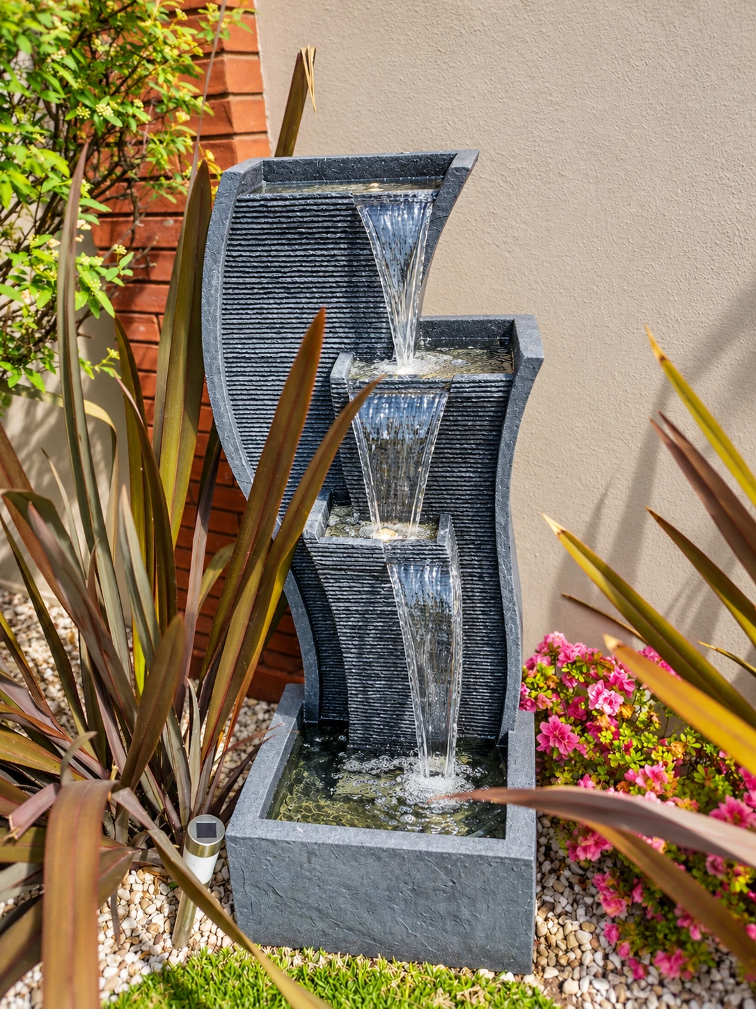 Fuente alta de tres caídas de agua entre plantas, como inspiración de ambientación