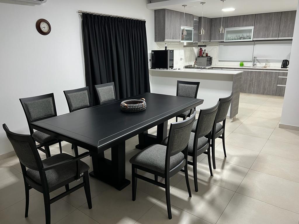 Mesa rectangular con sillas tapizadas frente a una cocina con barra.