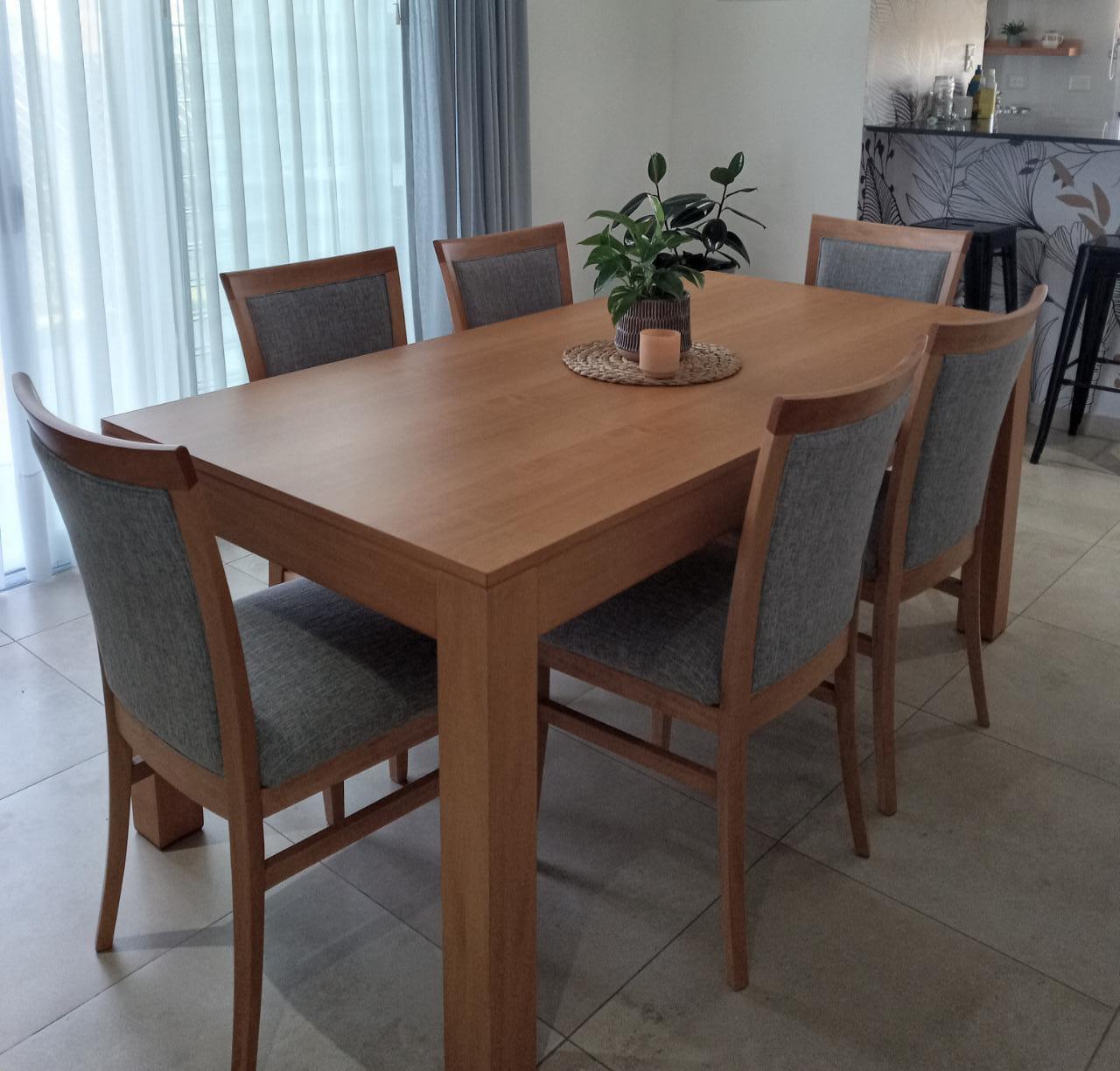Mesa rectangular con sillas tapizadas y una planta en el centro.